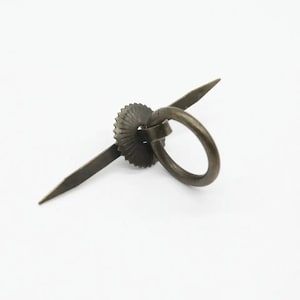 May include: A brass ring pull with a decorative, scalloped, circular base and a long, thin, pointed handle.