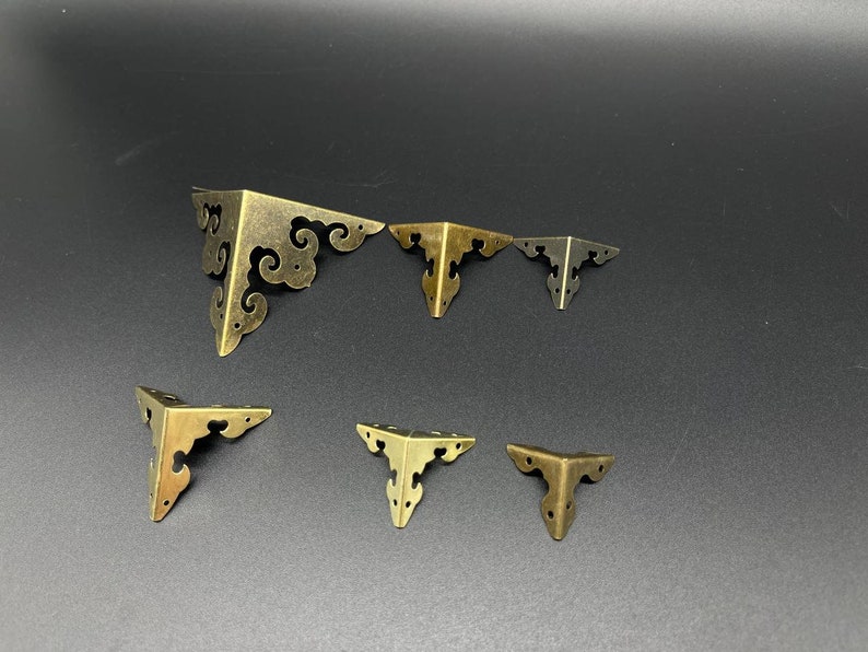 May include: Set of six antique gold corner brackets with ornate designs. The brackets are in various sizes and are perfect for adding a decorative touch to furniture or crafts.