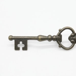 Puede incluir: Una llave de estilo antiguo con un lazo en forma de corazón y detalles ornamentados. La llave está hecha de metal y tiene un acabado bronce.