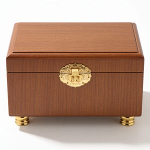 May include: A rectangular wooden jewelry box with a medium brown wood grain finish. The box features a gold-colored metal latch with an ornate, scalloped design on the front and four small, rounded gold-colored metal feet at the base.