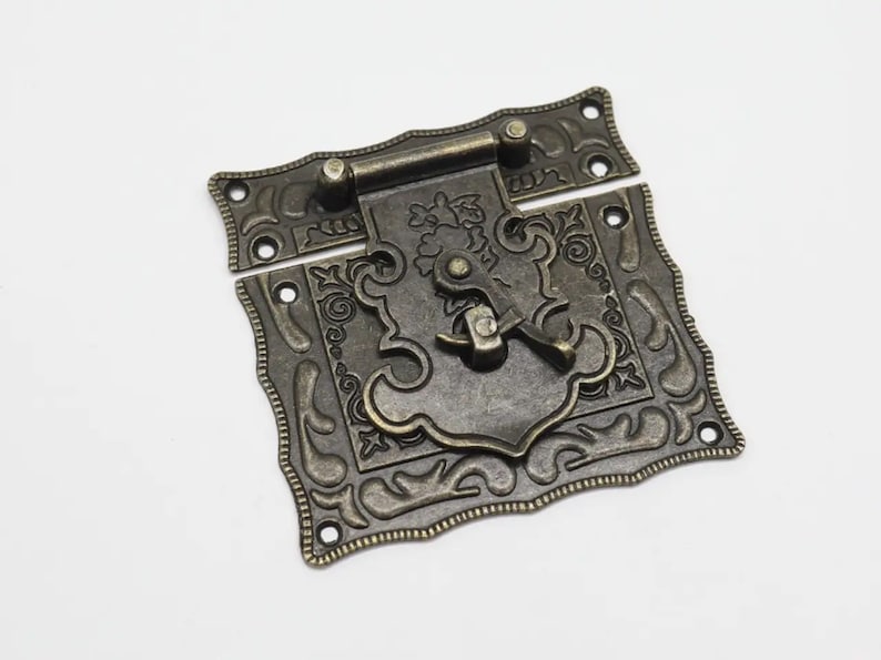 May include: A rectangular bronze-toned metal latch with an antiqued finish, featuring intricate embossed scrollwork and floral patterns. The hardware includes a hinged top plate with mounting holes and a central rotating locking mechanism.