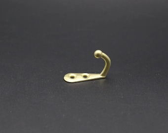 May include: A gold-toned metal hook with a rounded top and two screw holes. The hook is designed for hanging items on a wall.