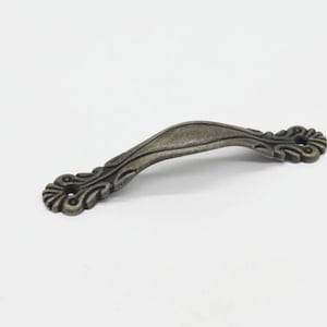 May include: A silver-toned metal cabinet pull with a decorative, ornate design. The pull has a curved shape and is designed for use on furniture.