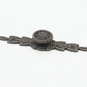 Könnte beinhalten: Antiker Bronze-Schrankgriff mit floralem Design und einem runden Knopf. Der Griff hat auf beiden Seiten des Knopfes ein blattartiges Design.