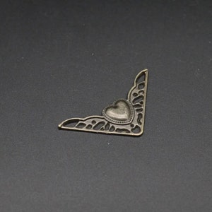 Puede incluir: Un adorno de esquina de bronce con un diseño de corazón decorativo. El corazón está en relieve y tiene una superficie texturizada.
