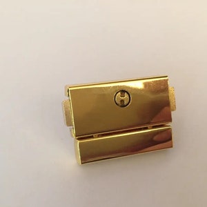 May include: Gold-toned metal watch band clasp with a small, round, engraved 'H' on the top.