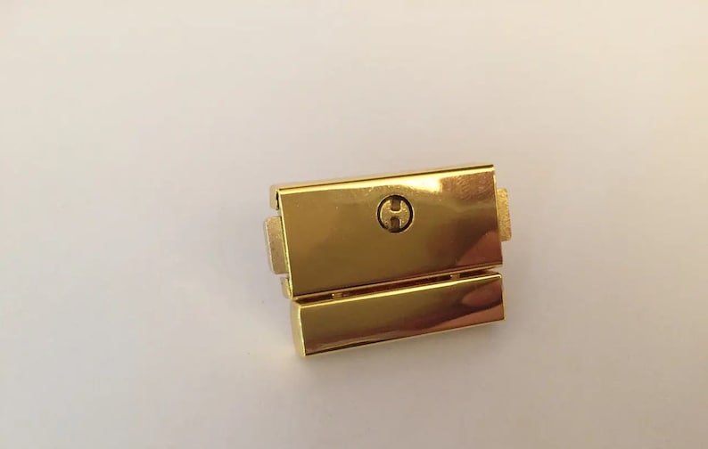 May include: Gold-toned metal watch band clasp with a small, round, engraved 'H' on the top.