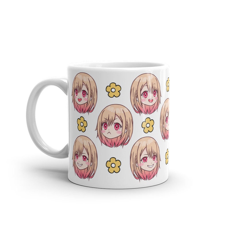 May include: White ceramic mug featuring a repeating pattern of a cartoon anime girl with blonde hair and pink cheeks. The girl has different facial expressions and is surrounded by yellow flowers.