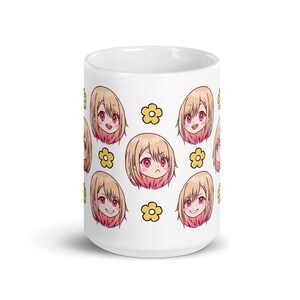 May include: White ceramic mug featuring a repeating pattern of a cartoon anime girl with blonde hair and pink cheeks. The girl has different facial expressions. The background is white with yellow flower accents.