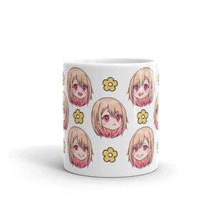 May include: White ceramic mug featuring a repeating pattern of a cartoon anime girl with blonde hair and pink cheeks. The girl has different facial expressions. The background is white with yellow flowers.
