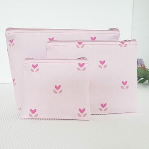 Op de afbeelding: Set van drie roze ritszakjes met een roze en wit bloemenpatroon. De zakjes zijn in elkaar genest, met het grootste zakje onderaan en het kleinste zakje bovenaan.