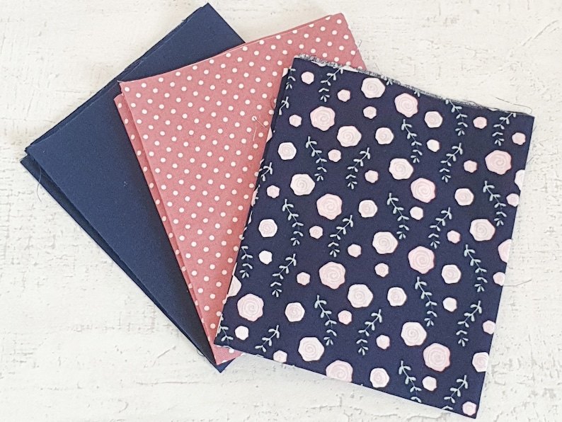 May include: Three fabric swatches in navy blue, dusty rose with white polka dots, and navy blue with a floral pattern. The floral pattern features pink roses and white leaves. Suitable for sewing and craft projects.