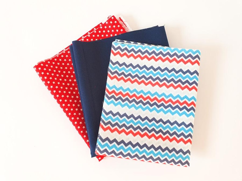 May include: A selection of fabric pieces in red, navy blue, and patterned designs. One fabric is red with white stars, another is solid navy blue, and the third features a chevron pattern in red, blue, and white. Suitable for sewing and craft projects.