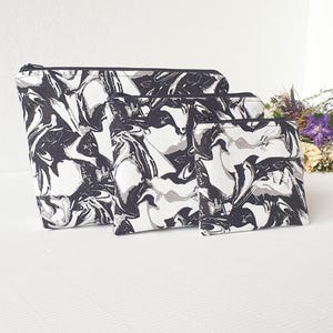 Op de afbeelding: Set van drie zwarte en witte marmeren ritszakjes. De zakjes zijn in verschillende maten en hebben een modern, abstract ontwerp.
