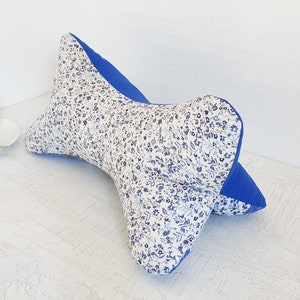 Op de afbeelding: Een blauw en wit kussen met bloemenprint en een blauwe achterkant. Het kussen is gevormd als een vlinderdas en is ontworpen om de nek te ondersteunen.