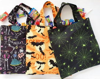 May include: Three Halloween trick-or-treat bags with different designs. One bag is black with a skeleton and fiesta design, another is orange with bats and the words "Boo!" and "Trick or Treat", and the last is black with green spiderwebs and spiders.