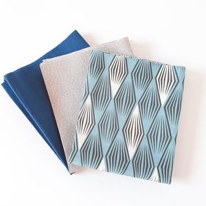 May include: Three fabric squares in blue, grey and patterned designs. The top square has a geometric pattern in light blue, black and white. The middle square is light grey with white polka dots. The bottom square is a solid navy blue.