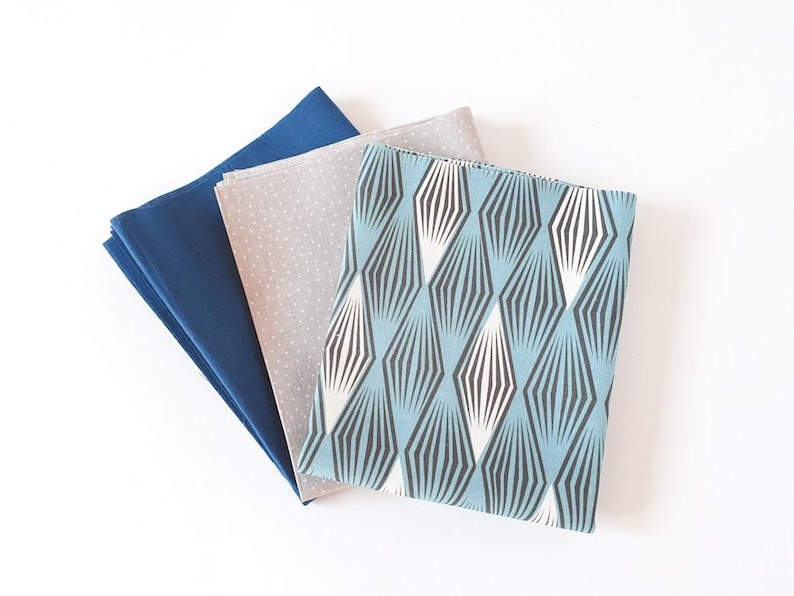 May include: Three fabric squares in blue, grey and patterned designs. The top square has a geometric pattern in light blue, black and white. The middle square is light grey with white polka dots. The bottom square is a solid navy blue.