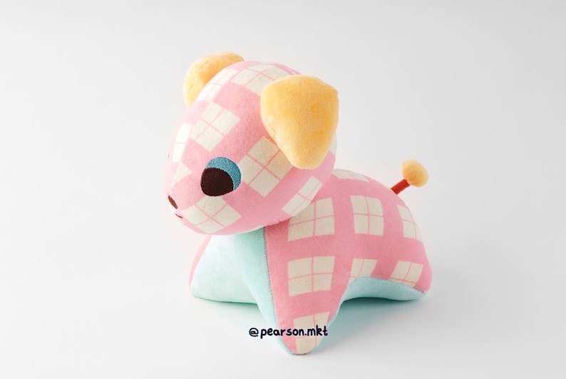 May include: Pink and white plaid plush toy dog with yellow ears and a red tail. The dog is sitting on a white background.