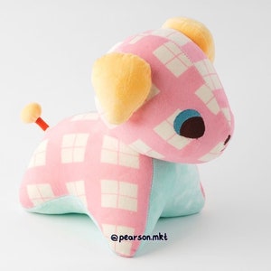 May include: A pink and white checkered plush toy dog with yellow ears and blue eyes. The dog is sitting on a white surface. The toy is made of soft, cuddly fabric and is perfect for cuddling.