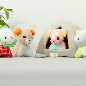 May include: Four plush toys, including a green and white dinosaur, a brown and white dog, a pink and blue dog, and a blue and yellow dog. The pink and blue dog is sitting inside a beige tent-shaped dog bed.
