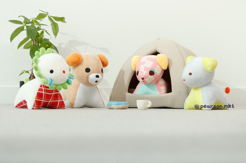 May include: Four plush toys, including a green and white dinosaur, a brown and white dog, a pink and blue dog, and a blue and yellow dog. The pink and blue dog is sitting inside a beige tent-shaped dog bed.