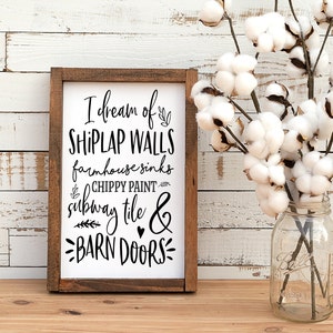May include: A wooden sign with the text "I dream of shiplap walls, farmhouse sinks, chippy paint, subway tile & barn doors" in black lettering on a white background.