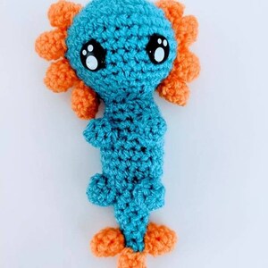 May include: A crocheted axolotl plush toy with a blue body and orange gills. The toy has large black eyes with white pupils.