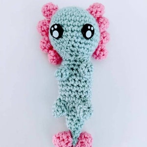 May include: A crocheted axolotl plush toy with a light blue body, pink frills, and black eyes.