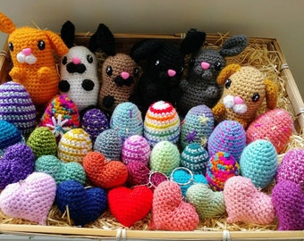 May include: A basket filled with crocheted Easter eggs, hearts, and small animal figurines. The eggs are in various colors and patterns, including striped, speckled, and floral. The hearts are mostly pink, purple, and blue. The animals include a bunny, a dog, and a cat.