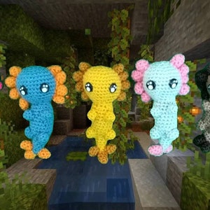 May include: Five crocheted axolotl plushies in different colors: pink, blue, yellow, light blue, and brown. The plushies are arranged in a row on a Minecraft-themed background.