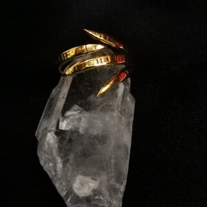 Op de afbeelding: Een gouden ring met een getextureerde, gehammerde afwerking. De ring is ontworpen met meerdere banden die naar boven en naar buiten buigen, waardoor een unieke en moderne look ontstaat. De ring wordt getoond op een helder kwartskristal.