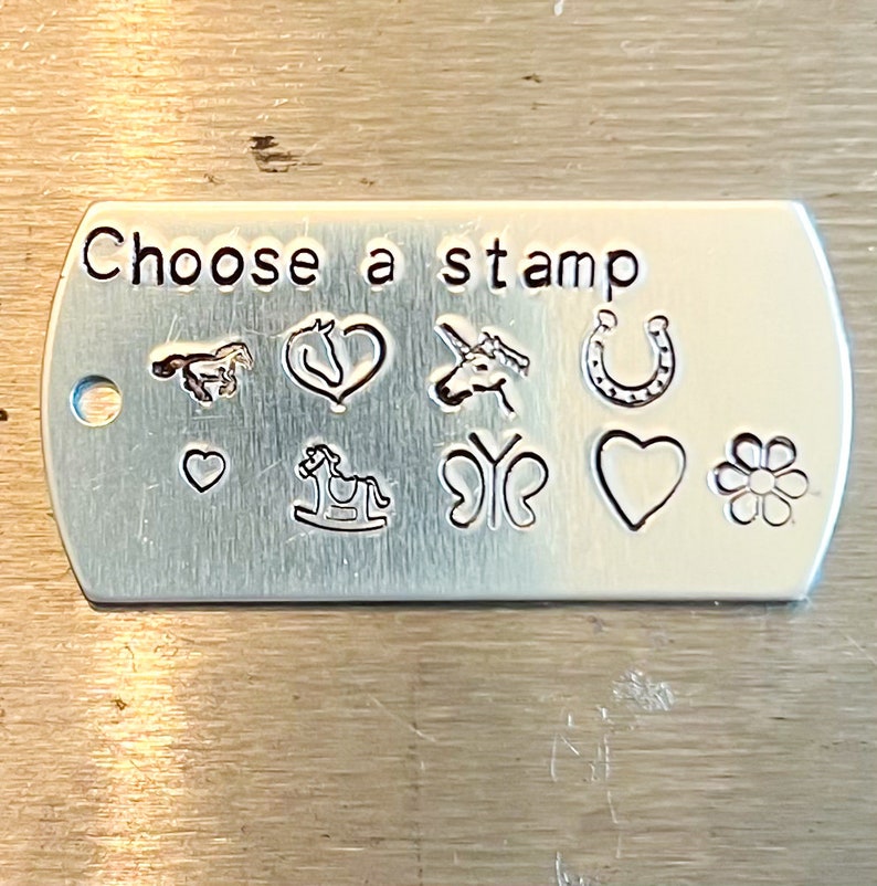 May include: A silver metal tag with the text "Choose a stamp" and a variety of stamp designs including a horse, heart, unicorn, horseshoe, rocking horse, butterfly, flower, and more.