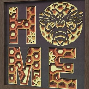 May include: A framed papercraft artwork with the word "HOME" in layered honeycomb patterns. A bee with intricate details is featured in the center, surrounded by honeycomb.