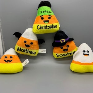 May include: Five Halloween-themed candy corn plush toys with different faces and names. The names are Christopher, Matthew, Sophie, and two unnamed candy corn toys.