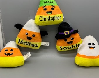 May include: Five Halloween-themed candy corn plush toys with different faces and names. The names are Christopher, Matthew, Sophie, and two unnamed candy corn toys.
