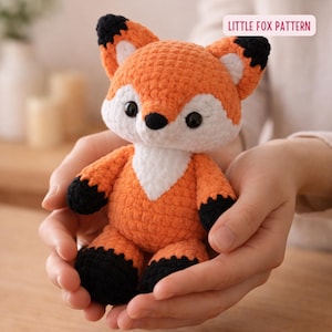 Puede incluir: Un juguete de zorro tejido a ganchillo en tonos naranja, blanco y negro. El zorro tiene pecho blanco, patas y orejas negras y ojos negros. El texto "LITTLE FOX PATTERN" está en un rectángulo rosa.