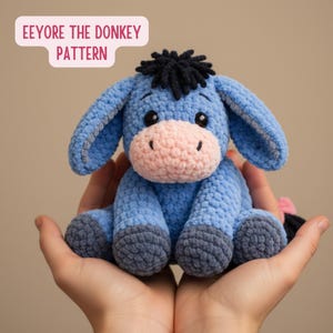 May include: A blue crochet donkey toy with a pink nose and grey hooves. The donkey has black eyes and a black mane. The text "Eeyore the Donkey Pattern" is in a pink bubble above the donkey.