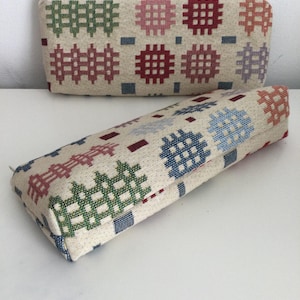 May include: Two fabric zippered pouches with a colourful geometric pattern. The pouches are made of a woven fabric with a cream background and red, green, blue, and pink geometric shapes.