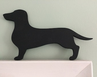 May include: Black silhouette of a dachshund dog, standing on a white surface.