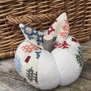 May include: A decorative, handcrafted pumpkin with a patchwork design. The pumpkin features a cream-coloured base with sections of patterned fabric in red, blue, and green. It has a wooden stem and fabric leaves, perfect for autumn decor.