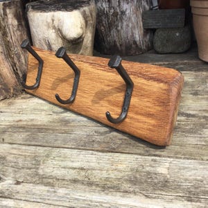 May include: A rectangular piece of light brown textured wood featuring three dark metal hooks shaped like railway spikes. Each hook is securely fastened to the wooden board with small screws, providing a sturdy arrangement for hanging items.