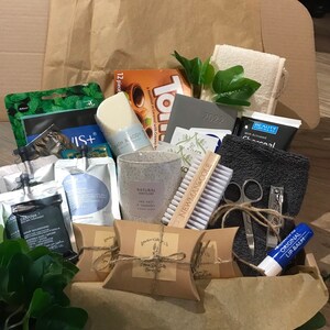 May include: A gift box filled with self-care items. Includes a candle, soap, bath products, lip balm, a nail brush, nail clippers, a washcloth, and a 2022 planner. The box also contains a package of chocolates and other beauty products.