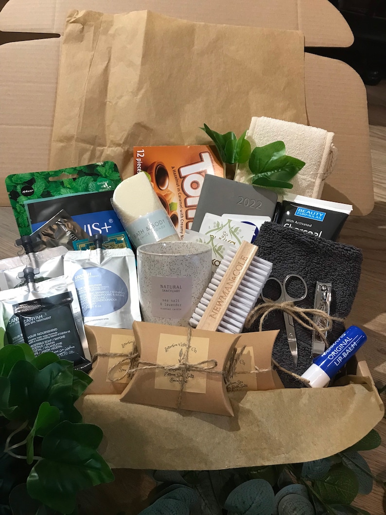 May include: A gift box filled with self-care items. Includes a candle, soap, bath products, lip balm, a nail brush, nail clippers, a washcloth, and a 2022 planner. The box also contains a package of chocolates and other beauty products.
