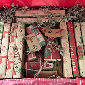 May include: A Christmas advent calendar box filled with wrapped gifts. The gifts are wrapped in festive paper with holiday designs and tied with twine. The box is lined with red paper and filled with decorative paper.