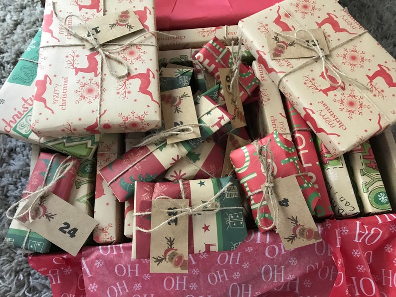 May include: A collection of wrapped Christmas gifts in a box. The gifts are wrapped in festive paper with reindeer, snowflakes, and Christmas tree patterns. Each gift is tied with twine and has a small tag. The color scheme includes red, green, and cream.