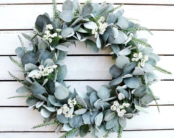 Può includere: Una ghirlanda di eucalipto verde e bianca con piccoli fiori bianchi. La ghirlanda è realizzata con verde artificiale ed è perfetta per uno stile di arredamento rustico o da fattoria.