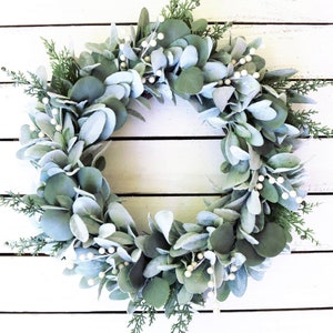 May include: A silver-green eucalyptus wreath with white berries, perfect for a farmhouse or rustic decor theme.