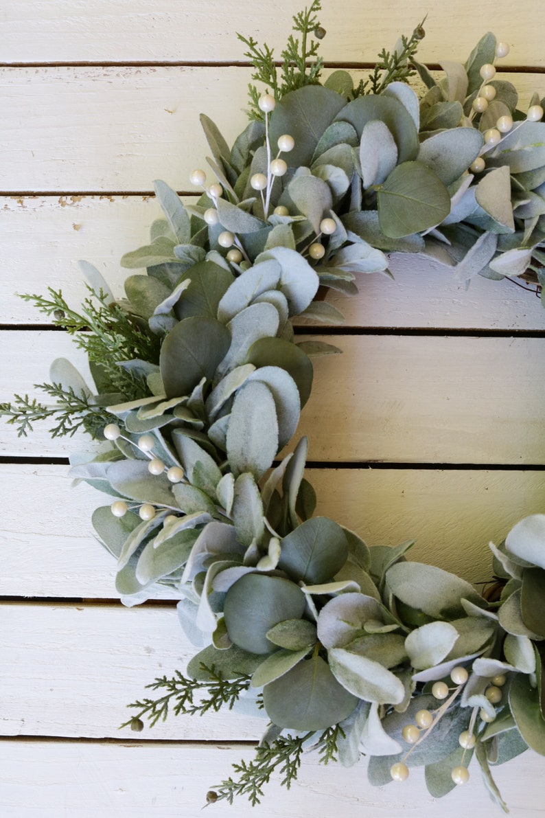 May include: A green and white eucalyptus wreath with white berries. The wreath is made of faux eucalyptus leaves and is perfect for a farmhouse or rustic decor style.