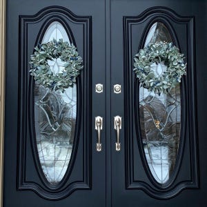 May include: A pair of black double doors with oval glass panels and silver door handles. Each door is decorated with a silver and green wreath.